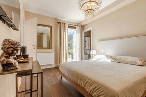 A bedroom with a bed, a desk with a statue, a chandelier, and a view through the open door. - Tenuta Le Scuderie del Palio - Agritourism in Tuscany among the horses (Siena)