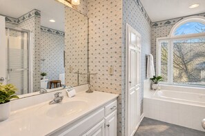 A bathroom with a large mirror, a sink, a bathtub, and a window. - Lakefront Retreat | Dock + Sunset Views (Prosperity)