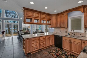 A modern kitchen with wooden cabinets, a dishwasher, and a large island. - Lakefront Retreat | Dock + Sunset Views (Prosperity)