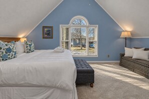 Ein Schlafzimmer mit einem großen Bett, einem Fenster mit Jalousien, einer Bank und einer Lampe.