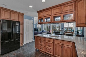 A kitchen with wooden cabinets, a black refrigerator, and a large island with drawers. - Lakefront Retreat | Dock + Sunset Views (Prosperity)