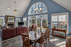A spacious living area with a fireplace, a television, and a dining table with chairs. - Lakefront Retreat | Dock + Sunset Views (Prosperity)