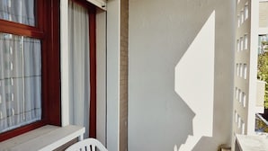 A balcony with a white chair, a window with curtains, and a shadow on the wall. - Functional and Comfortable Seafront Studio (San Michele al Tagliamento)