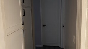 Un pasillo estrecho con una puerta blanca al final, una rejilla en el techo y un accesorio de iluminación.