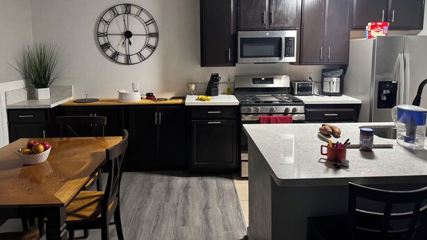 Una cocina moderna con gabinetes oscuros, una estufa de acero inoxidable, un microondas y un reloj en la pared.