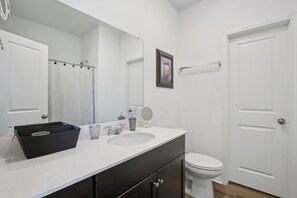 Un baño con un lavamanos blanco, un espejo, un inodoro y una cesta de almacenamiento negra.