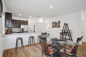 Una cocina moderna con armarios blancos, un refrigerador de acero inoxidable y una mesa de comedor de vidrio con sillas de metal.