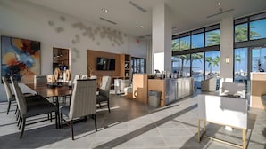 Un hall d’hôtel spacieux comprenant un espace repas, un comptoir d’accueil et de grandes fenêtres donnant sur des palmiers.