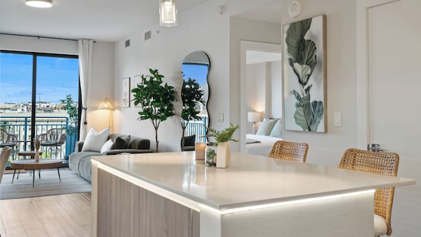 Un espace de vie moderne doté d’un îlot central, d’un coin repas et d’un balcon aménagé avec du mobilier d’extérieur.