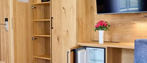 Un armario de madera con un mini refrigerador incorporado, un televisor de pantalla plana y un escritorio pequeño con una silla.