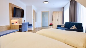 Une chambre d’hôtel avec deux lits, un téléviseur fixé sur un panneau en bois, un bureau avec une chaise et une grande fenêtre avec des rideaux.