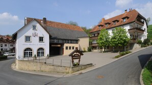 Un bâtiment traditionnel, avec une enseigne indiquant « Kleines Bauernhaus in Niedersdorf », une rue pavée et un ciel dégagé.