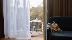 Une pièce avec un balcon, une table sur laquelle se trouvent une tasse et une soucoupe blanches, et un canapé sombre agrémenté de coussins à motifs.