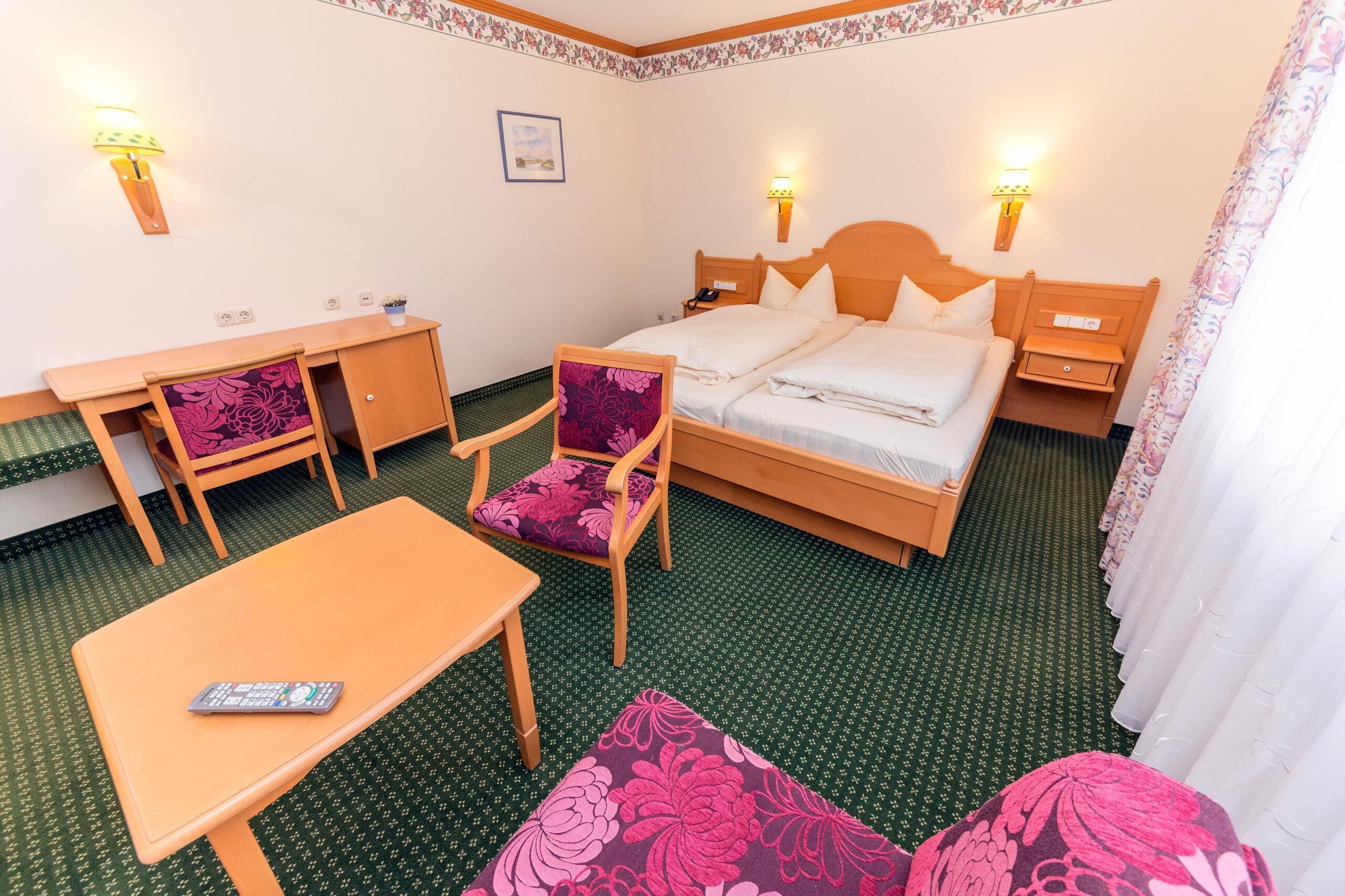 A hotel room with a bed, a desk, a chair, a table, and a small rug.