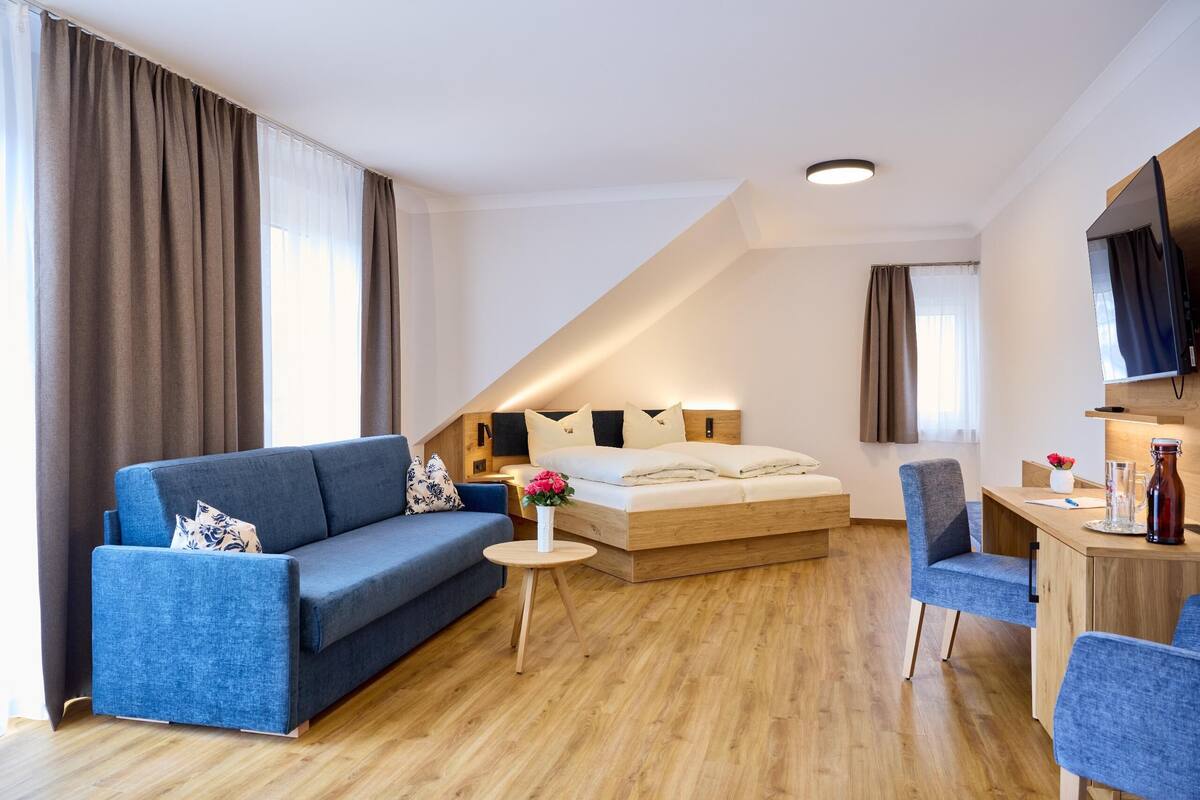 A modern hotel room with a sofa, a small round table, a bed, and a desk area.