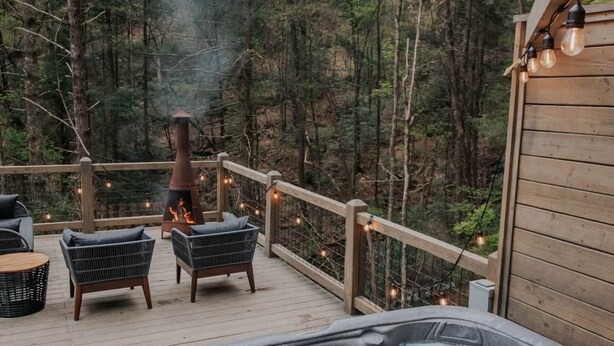A hot tub on a wooden deck with outdoor seating, surrounded by a forest.