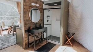 A modern bathroom with a wooden vanity, a round mirror, a black sink, and a glass shower enclosure.