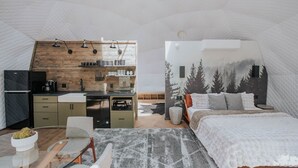 An interior with a kitchenette, a bed, and a wall with a forest mural.