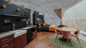 Un interior moderno con cocina, comedor y zona de descanso, destacando un diseño geométrico en el techo y grandes ventanales.