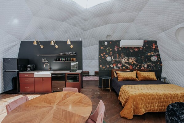 A compact, modern room with a kitchenette, a bed with a floral headboard, a dining table, and a unique geometric ceiling. - Glamp Blue Ridge - Dome 7 Amelia (Gilmer County)