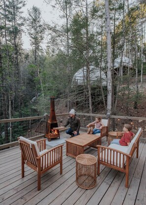 Una terraza con mobiliario de madera, una estufa de leña y vistas al bosque.