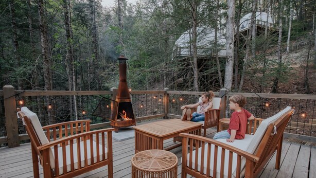 A wooden deck with wicker furniture, a fire pit, and string lights.