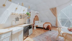 A compact, modern room with a kitchenette, a bed, and a large window.