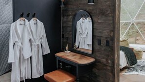 Una habitación con tocador de madera, un espejo y dos albornoces blancos colgados en un perchero.
