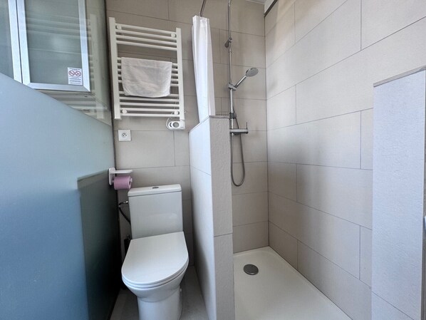 Um banheiro pequeno e moderno, com vaso sanitário, chuveiro e porta-toalhas.