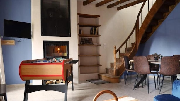 Una sala de estar acogedora con mesa de fútbol, chimenea, escalera y comedor con sillas y mesa.
