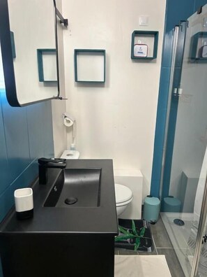 Une salle de bain moderne avec un lavabo noir, un miroir, des toilettes et un espace douche.