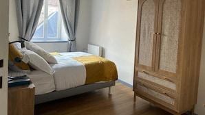 Un dormitorio con cama, armario de madera, radiador y ventana con cortinas.