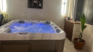 Un jacuzzi con luces LED azules, un estante de madera con adornos y una planta en maceta.