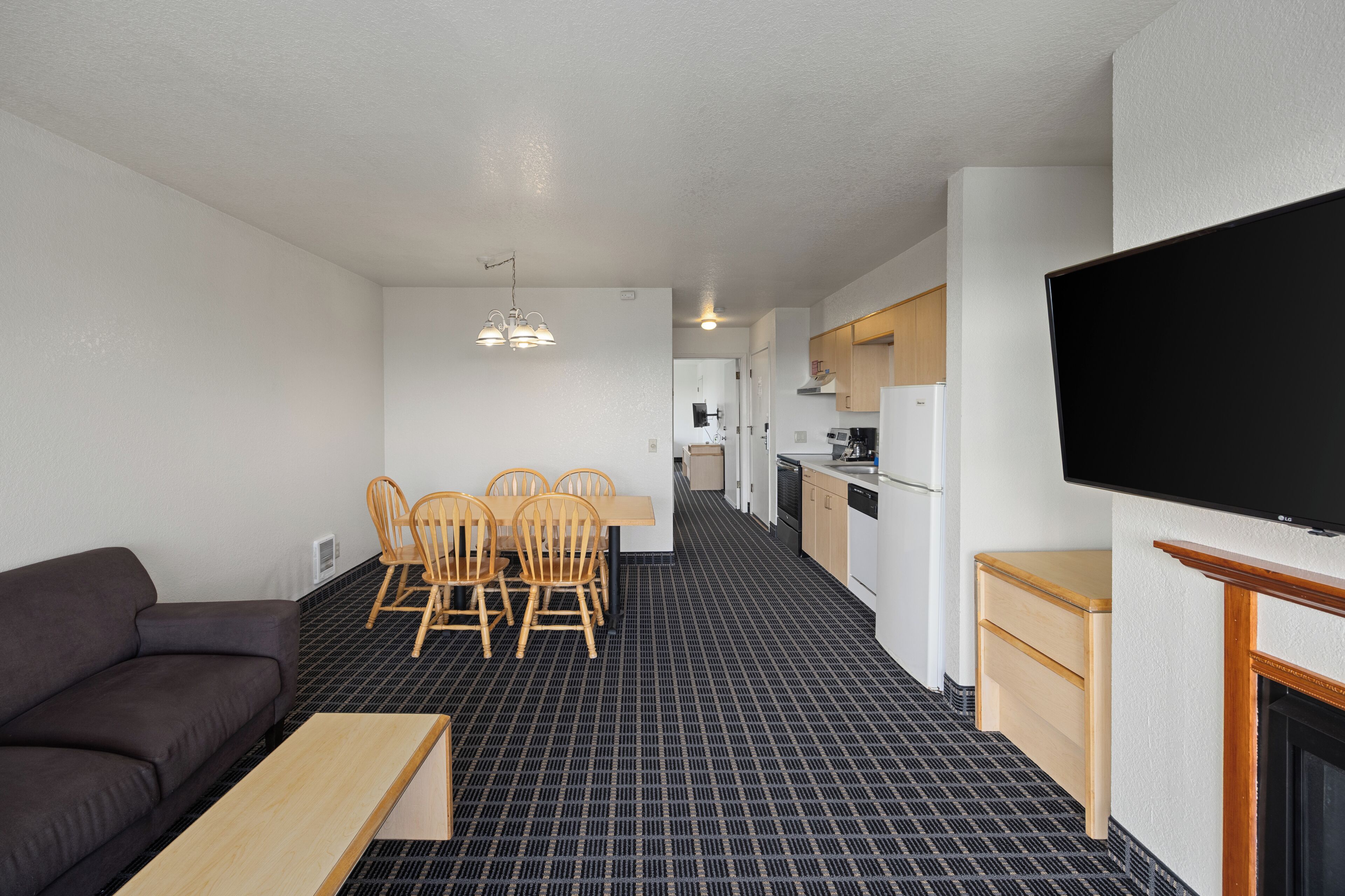 Un espacio habitable compacto con sofá, mesa de comedor, sillas, kitchenette y televisor montado en la pared.
