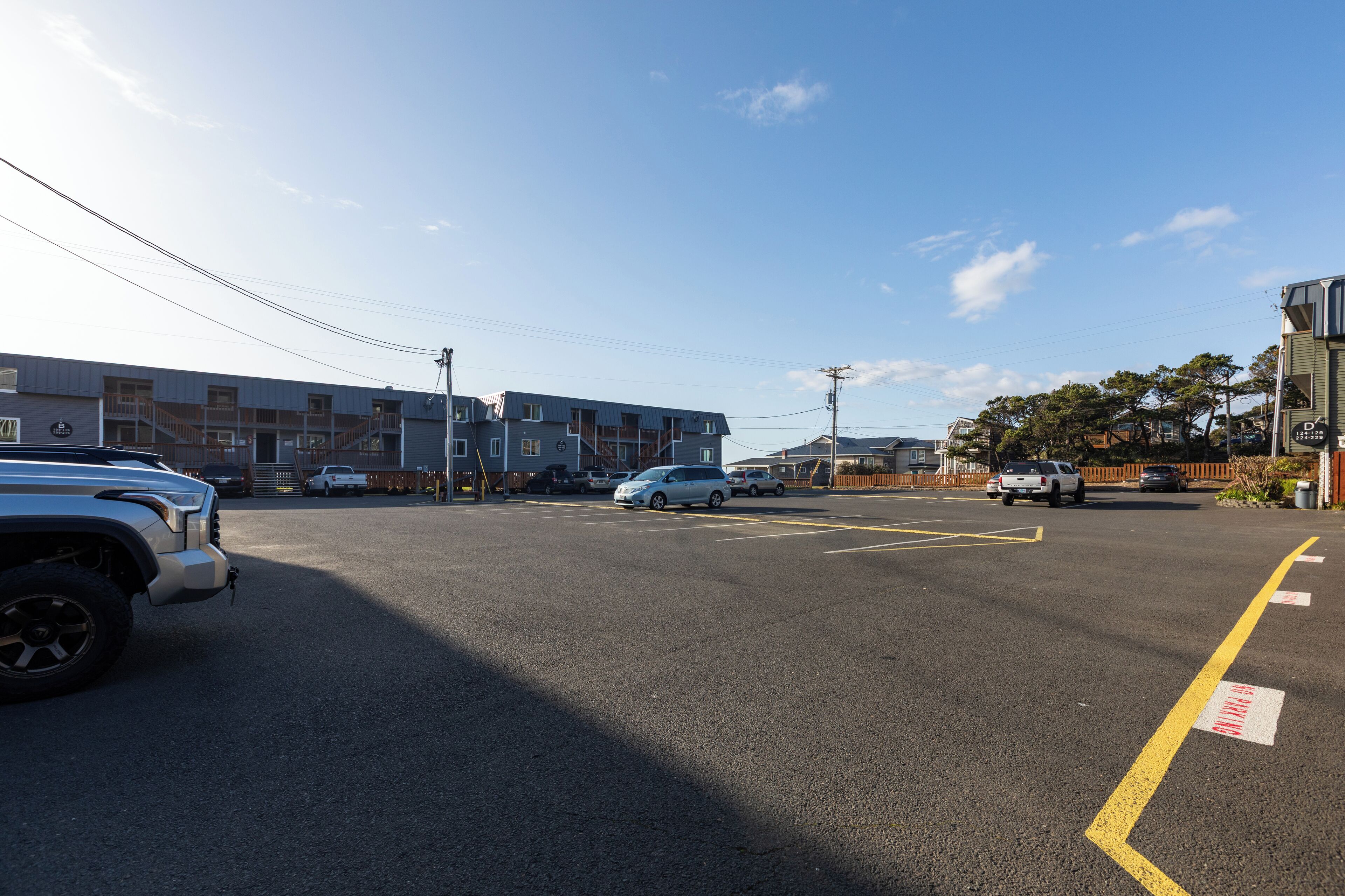 A parking lot with vehicles, a building with multiple floors, and a clear sky.