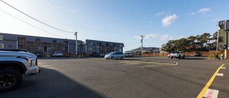A parking lot with vehicles, a building with multiple floors, and a clear sky.