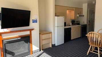 A compact hotel room with a kitchenette, a television, a fireplace, and a patterned floor.