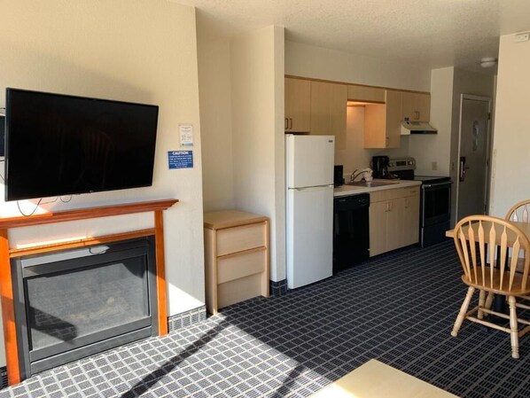 A compact hotel room with a kitchenette, a television, a fireplace, and a patterned floor. - Surfside Resort (Rockaway Beach)