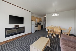 Un espace de vie compact doté d’un téléviseur à écran plat fixé au mur, d’une cheminée intégrée, d’un coin repas avec des chaises en bois et d’une petite cuisine en arrière-plan.