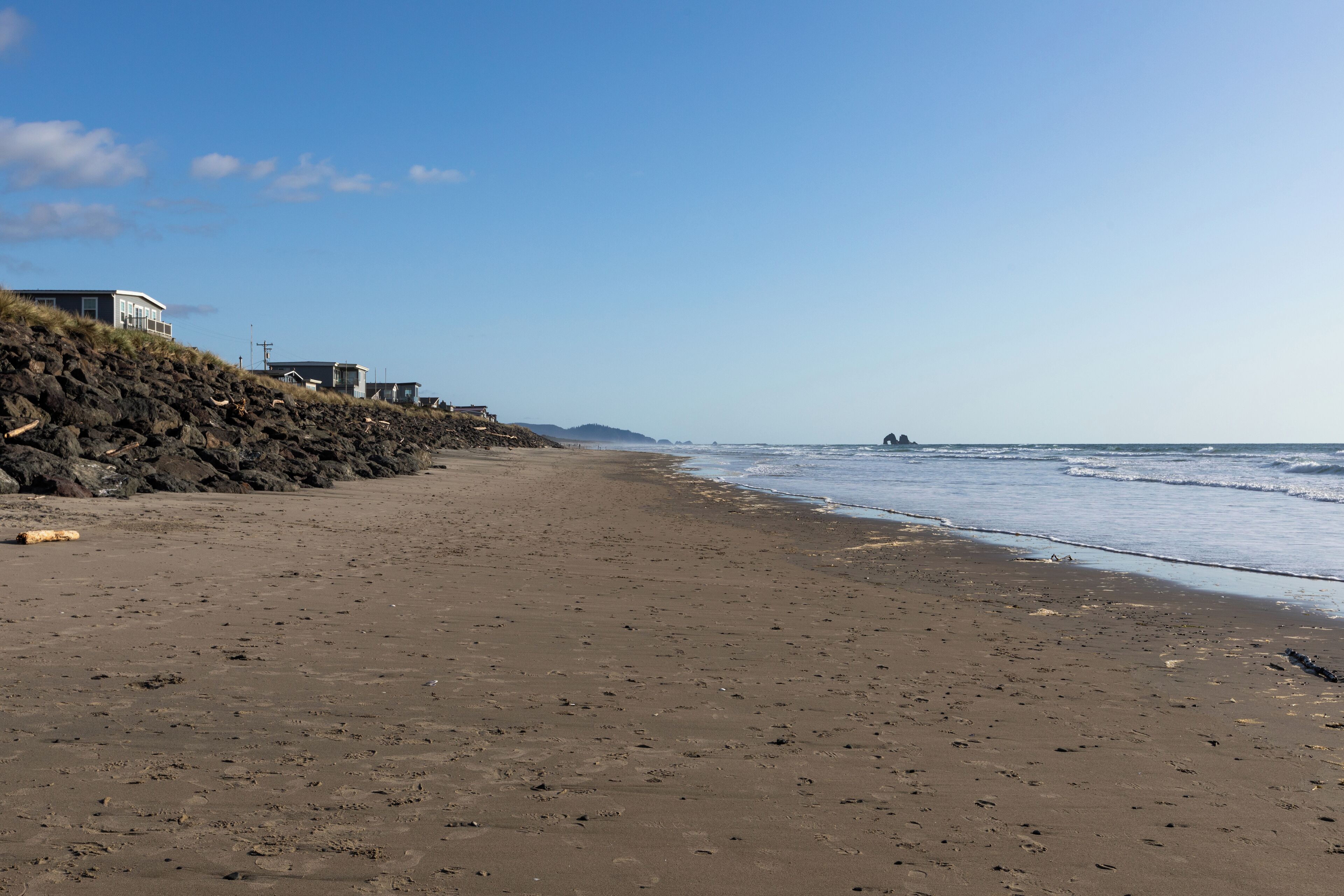 A beach with a rocky shoreline, a few buildings, and the ocean in the background.