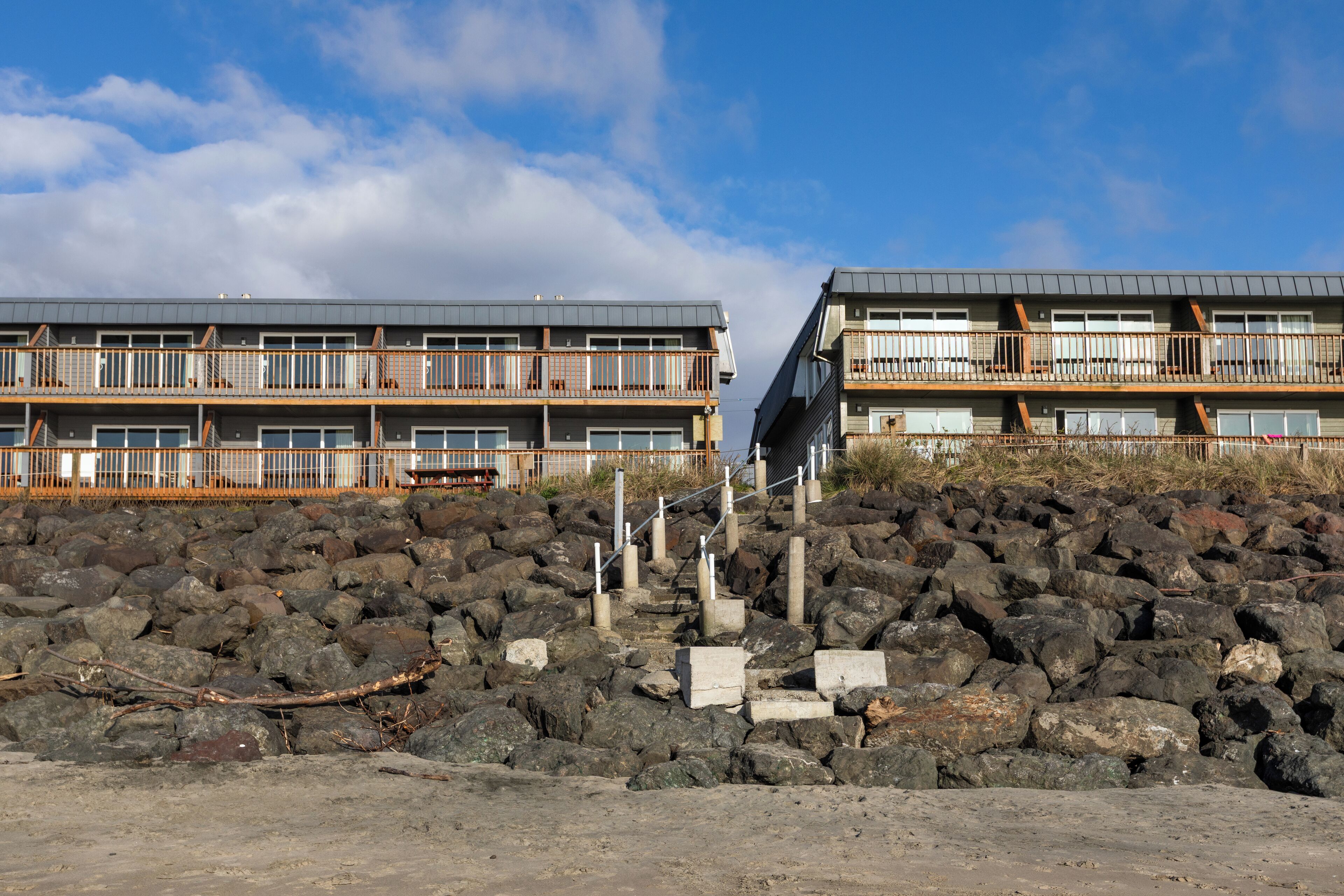 A coastal building with multiple balconies, a rocky foreground, and a clear sky.