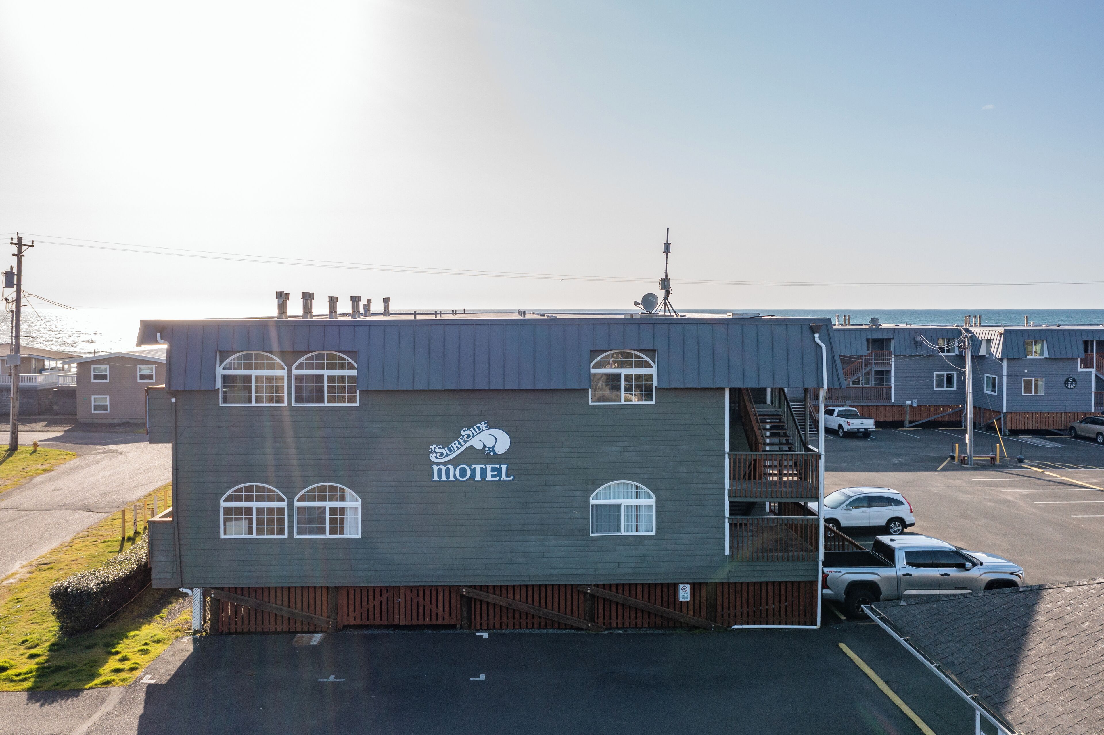 A motel with a sign, a parking lot, and a view of the ocean.