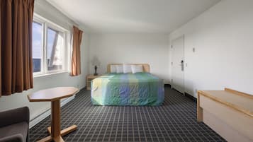 Une chambre d’hôtel avec un lit, un bureau, une chaise, une fenêtre avec des rideaux et une porte.