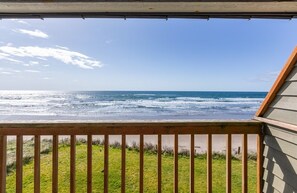 Une vue depuis un balcon donnant sur l’océan, avec une balustrade en bois et une structure de bâtiment.