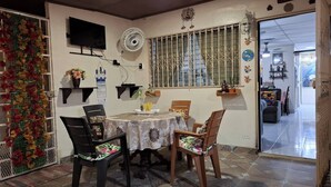 Een eetruimte met een tafel, stoelen, een decoratieve wand, een ventilator en zicht op een andere kamer.