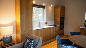 Eine moderne Küche mit Holzschränken, einer eingebauten Spüle und einem Fenster. Im Essbereich befinden sich zwei blaue Stühle und ein runder Tisch.