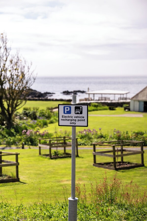 Señal de punto de carga para vehículos eléctricos en un parque con mesas de picnic y vistas al mar.