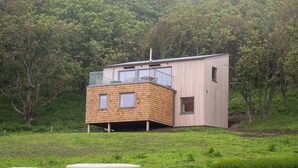 Ein modernes Haus mit Holzfassade, ein Auto und ein Golfwagen vor der Einfahrt.