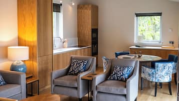 A modern kitchen with wooden cabinets, a dining area with patterned chairs, and a large window with a view of greenery.