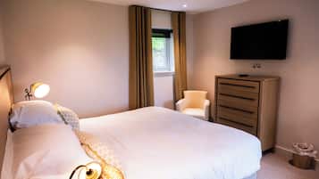 A hotel room with a bed, a TV mounted on the wall, a dresser, a chair, and a window with curtains.
